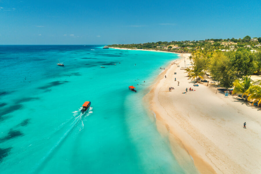 Aerial view of boats on tropical sea coast with sandy beach at sunny day. Summer holiday on Indian Ocean, Zanzibar, Africa. Landscape with boat, palm trees, transparent blue water, hotels. Top view