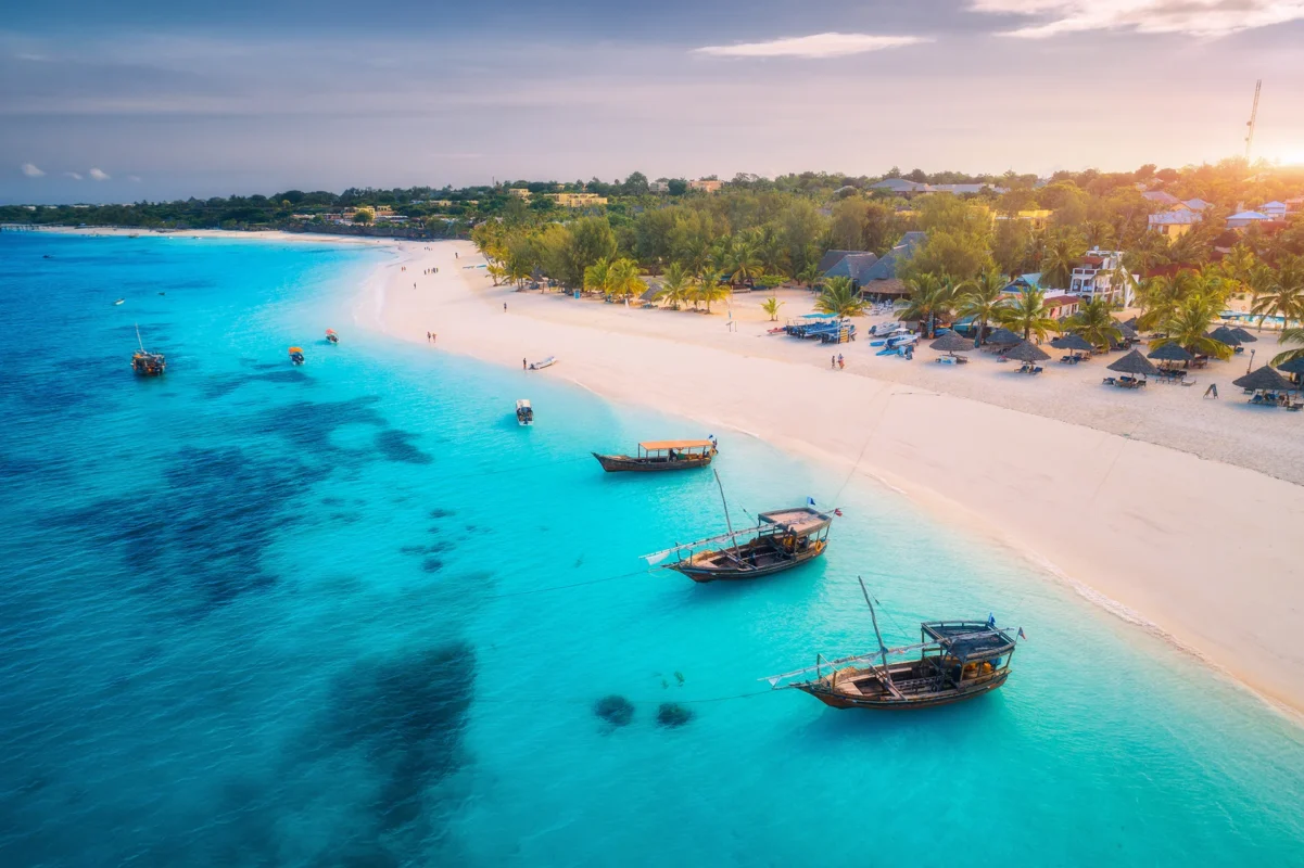 Aerial view of the fishing boats on tropical sea coast with white sandy beach at sunset. Summer holiday on Indian Ocean, Zanzibar