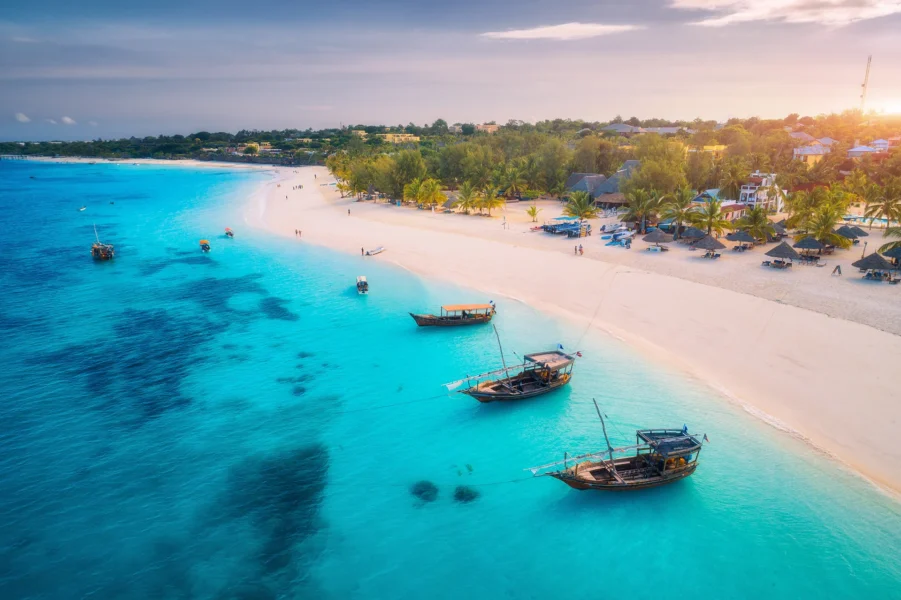 Aerial view of the fishing boats on tropical sea coast with white sandy beach at sunset. Summer holiday on Indian Ocean, Zanzibar